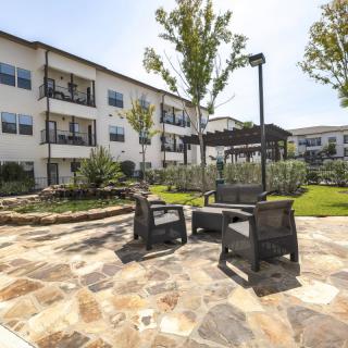 An outdoor patio area with seating and landscaping in front of a multi-story building on a sunny day.