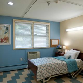 A cozy bedroom with blue walls and a single bed, featuring a window, lamp, and patterned decor.