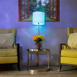A cozy living room setup featuring yellow armchairs, a stylish table lamp, and a vase of flowers, all against a softly lit purple wall.