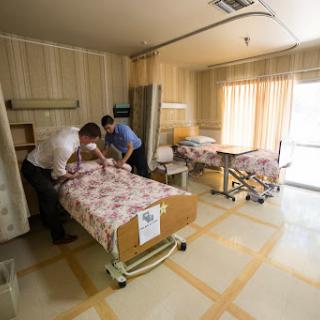 Two medical staff members preparing patient beds in a hospital room.