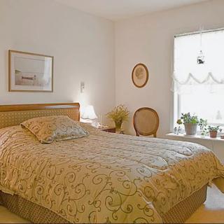 A cozy bedroom with a neatly made bed, window adorned with plants, and tasteful decor.