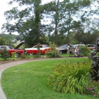Classic cars displayed in a garden setting at an outdoor car show.