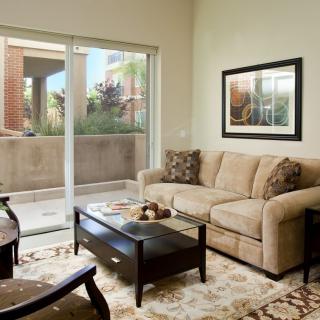 A cozy living room with a beige sofa, coffee table, and artwork, featuring a sliding glass door leading to an outdoor area.