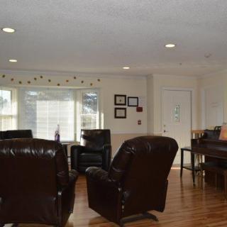 A cozy living room with leather armchairs, wood flooring, and a piano.