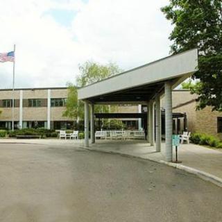 Entrance of a modern building with a flag and trees in the background.