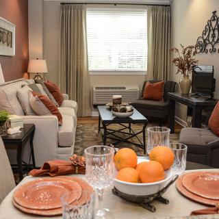 A cozy living room with warm orange accents, featuring a sofa and a dining table set with plates and glasses.