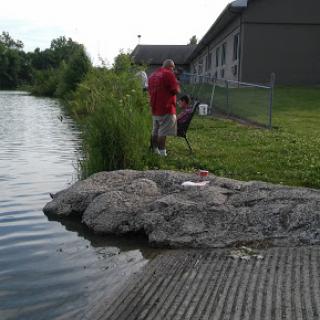A person fishing at the edge of a serene body of water, surrounded by lush greenery.