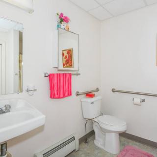 A brightly lit bathroom with pink accents, featuring a sink, toilet, mirror, and towel rack.