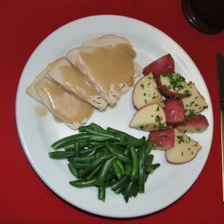 A dinner plate featuring turkey with gravy, green beans, and seasoned potatoes.