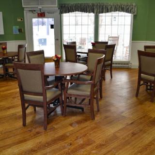 A cozy dining area featuring wooden tables and chairs, surrounded by green walls and large windows.