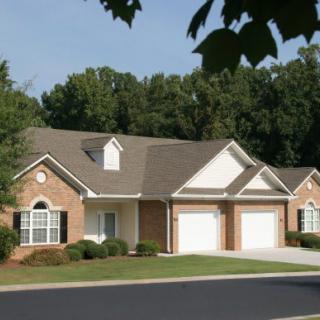A suburban house with a two-car garage and brick exterior set against a backdrop of trees.