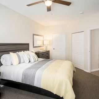 A modern bedroom with a neatly made bed, ceiling fan, and minimalist decor.