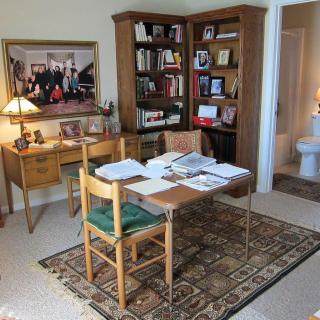 A home office with a desk covered in papers, surrounded by bookshelves and decorations.