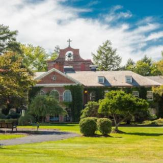 An ivy-covered historic building with a cross, surrounded by trees and greenery under a blue sky.
