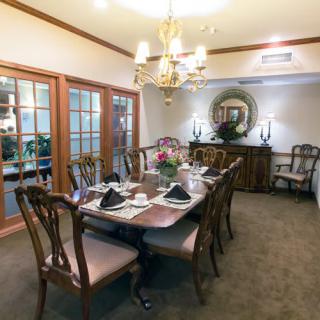 An elegant dining room setup featuring a long table with chairs, adorned with a chandelier and decorative elements.