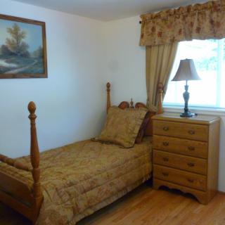 A cozy bedroom with a single wooden bed, matching dresser, and a lamp by the window.