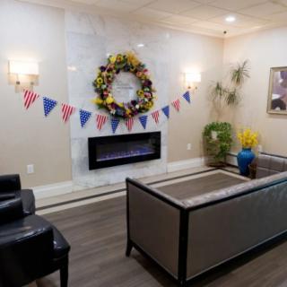 A cozy living room with a modern fireplace, adorned with a floral wreath and patriotic bunting, complemented by sleek furniture and indoor plants.
