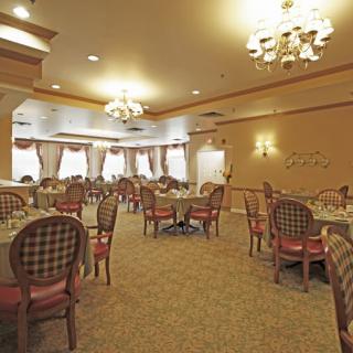 An elegant dining room with chandeliers, featuring neatly arranged tables and chairs on a carpeted floor.