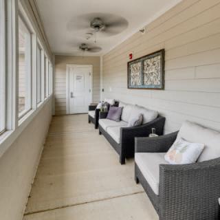 A cozy sunroom with rattan furniture and ceiling fan overlooking the outside through large windows.