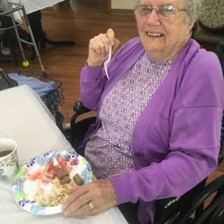 An elderly woman enjoying dessert at a social gathering.