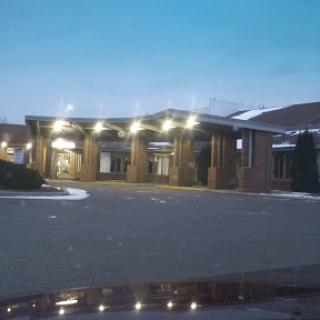 A hotel entrance captured during the evening, showcasing warm lights and a quiet parking area.