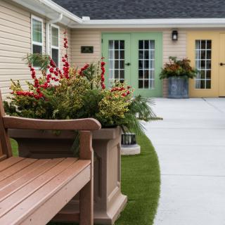 A cozy patio with a wooden bench, vibrant plants, and colorful doors.