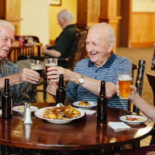 A group of elderly friends enjoying beer and conversation at a restaurant.