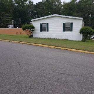 A mobile home situated on a quiet suburban street, surrounded by green lawns and trees.