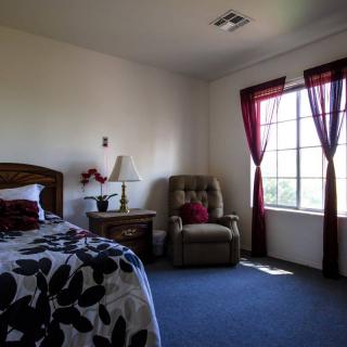 A cozy bedroom featuring a bed, armchair, and a large window with red curtains.