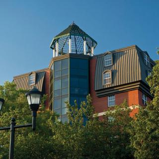 A uniquely designed building with modern architectural elements, surrounded by trees and set against a clear blue sky.
