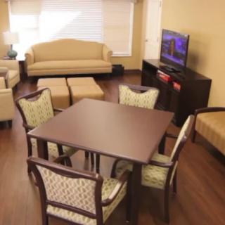 A cozy living room with a wooden dining table, upholstered chairs, and a TV.