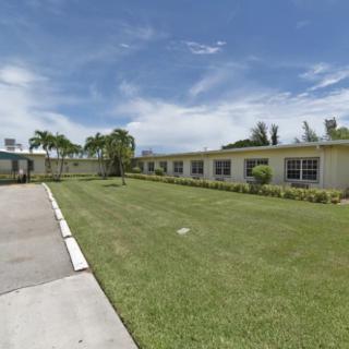 A one-story building with a well-maintained lawn and trees under a clear blue sky during the day.