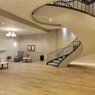 A modern lobby with a curved staircase and wooden flooring.