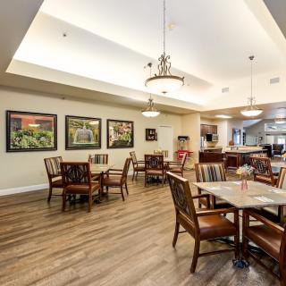 A spacious dining area with several wooden tables and chairs, decorated with framed wall art and illuminated by elegant ceiling lights.