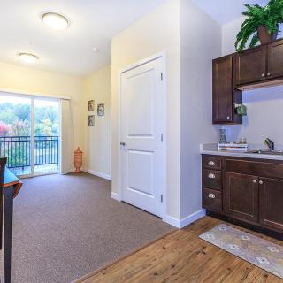 Bright and open interior space with kitchen cabinets, a sliding door leading to a balcony, and wood flooring.

