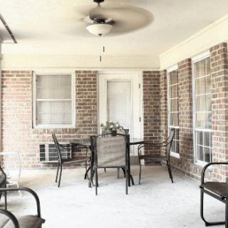 A cozy patio with a table, chairs, and a ceiling fan, surrounded by brick walls.