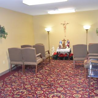 A small chapel with chairs, a crucifix, and decorated with lamps and floral arrangements.