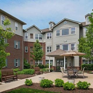 A residential building with a landscaped garden and patio area, featuring outdoor furniture and greenery.