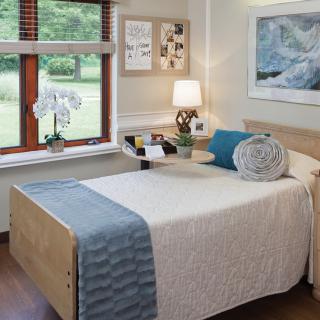 A cozy bedroom with a neatly made bed, a lamp on the bedside table, and an orchid by the window.