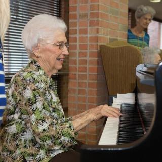 An elderly woman playing the piano indoors.