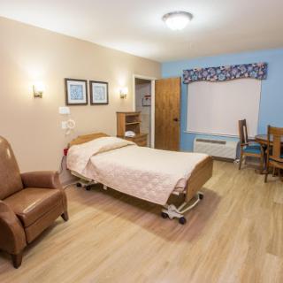 A cozy and well-lit hospital room featuring a bed, chair, and a small dining area.
