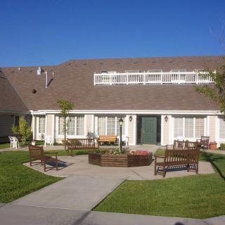 A two-story house with a well-maintained lawn, benches, and a clear blue sky.