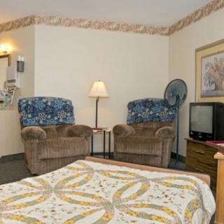 A cozy hotel room with a bed, two chairs, a television, and a lamp.