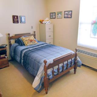A cozy bedroom featuring a single wooden bed with blue bedding, decorated with wall art and a carpeted floor.