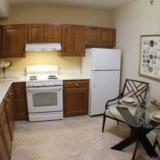 A cozy kitchen with wooden cabinets, a stove, refrigerator, and a small dining table.