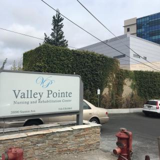 A sign for Valley Pointe in front of a building with ivy-covered walls and parked cars.