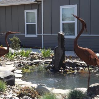 A garden scene with a pond, surrounded by decorative bird statues and landscaping elements.