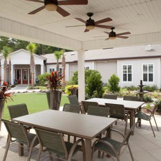A covered outdoor patio with dining tables and chairs, overlooking a landscaped garden.