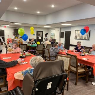 A group of seniors enjoying a festive indoor celebration with colorful balloons and decorated tables.