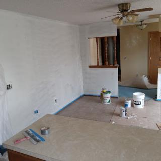 An unfinished living area undergoing renovation with paint supplies and a ceiling fan.
